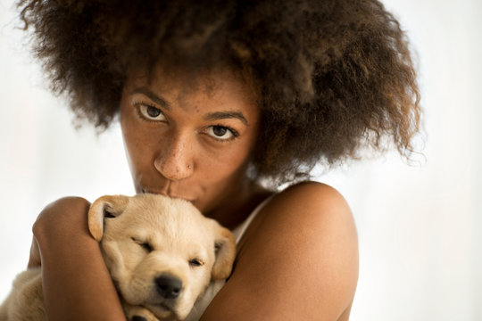 Young woman kissing her Labrador puppy.