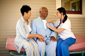 Nurse sitting on the deck of rest-home with elderly patients and listening to their heartbeat with stethoscope.