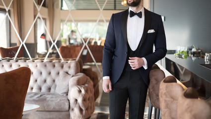 Man in expensive custom tailored suit, tuxedo standing and posing inside luxury apartment