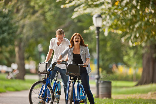 Smiling young couple riding bikes through a city park.