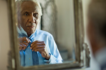 Senior man fixing his tie in the mirror.