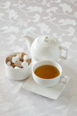 Afternoon tea service with hot tea cup, sugar cubes, and tea pot on white linen table cloth