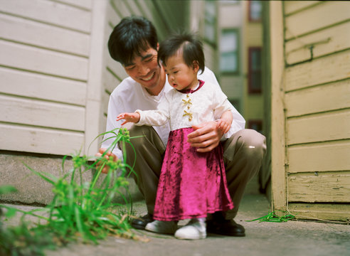 A man and a small girl are admiring a plant outside a house.