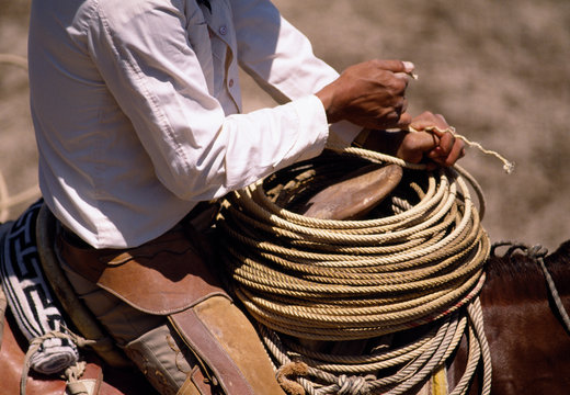 Cowboy holding a coil of rope at the front of his saddle.