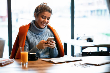Happy businesswoman typing text message on coffee break in a cafe.