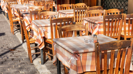 Greek outdoors tavern, empty tables and chairs, sunny day, city center