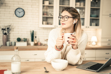 Peaceful good-looking woman in clear glasses holding glass of tea