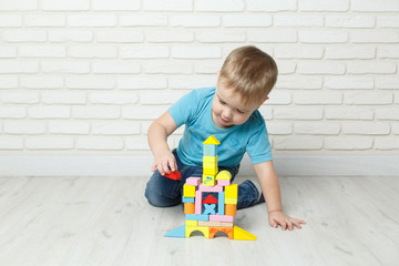 Little boy playing with a plastic constructor on a white background. Baby boy playing with blocks toys isolated on white background. Smiling baby is playing sitting on the floor developing toy.