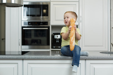 little funny boy eating a bun in the kitchen. cute baby eating baguette. Portrait of cute baby with bread in her hands. boy eat lunch in the kitchen