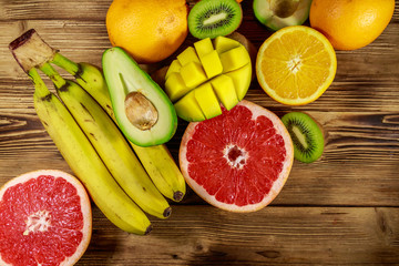 Assortment of tropical fruits on wooden table. Still life with bananas, mango, oranges, avocado, grapefruit and kiwi fruits