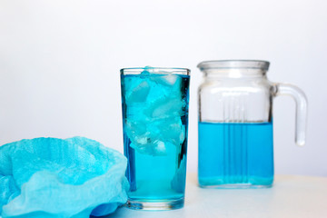 Glass with a blue cocktail with ice on a white background. © Elena
