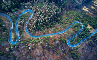 The aerial view of winding road from high mountain pass with trees in Transylvania, Romania, Curved road view by drone in the autumn-winter time