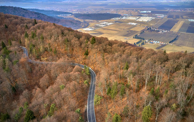 The aerial view of winding road from high mountain pass with trees in Transylvania, Romania, Curved road view by drone in the autumn-winter time