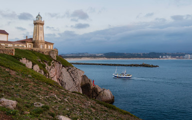 Fototapeta na wymiar Fishing boat entering during sunset,sailing in front of the lighthouse of Saint Juan, to the port