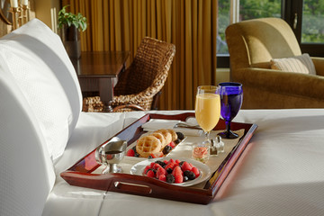 Breakfast room service tray on bed  in morning sunlight