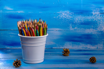 Colored pencils on a blue wooden background. Art Lifestyle concept. Background with soft selective focus. Educations concept, back to school concept. Gold bumps, a ray of sunshine and white bucket