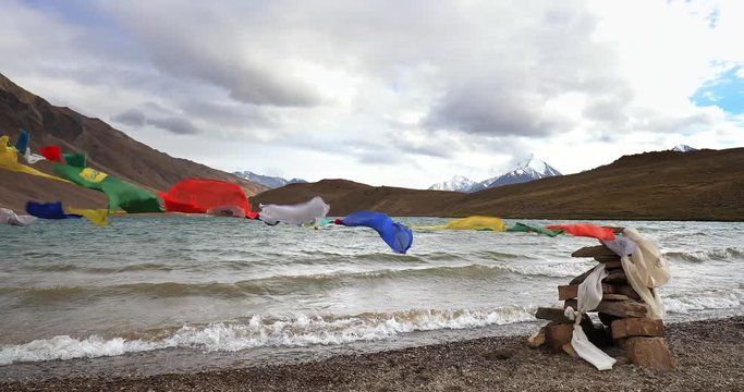 Traveling to Himalaya video landscape background. Buddhist prayer flags and waves of Chandra Tal lake 4K 60p