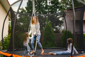 Mother and two daughters jumping on the trampoline, laughting and having fun at the yard outdoor.