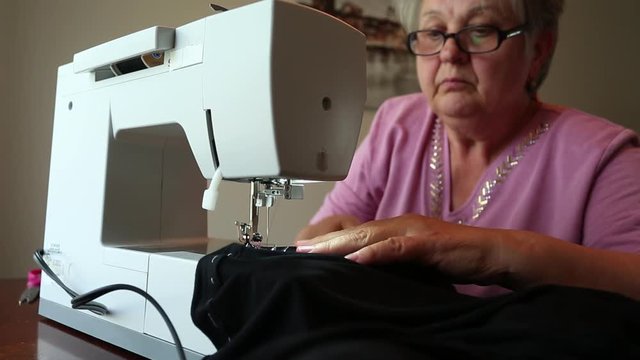 Close up of Hands of Hardworking European Elderly Woman, stitching fabric using Sewing Machine at her Workshop, Focused on working Process. Clothing, Design, dressmaking and tailoring