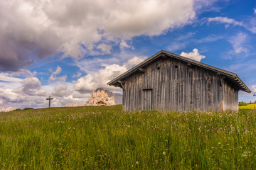 Obraz premium Alpe di Siusi, Seiser Alm with Sassolungo Langkofel Dolomite, an old barn in a grassy field with clouds in the sky