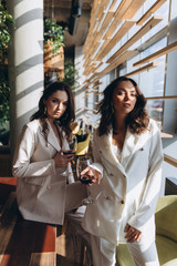 Two stylish sexy glamour elegant women wear white suits in a restaurant with a glass of wine.