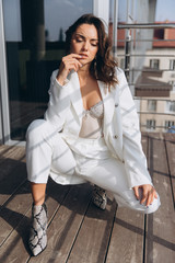 Fototapeta premium Beautiful young sexy woman, glamour girl in the white elegant jacket, corset, suit, makeup pastel tone lipstick, nails on the office balcony with the urban background.
