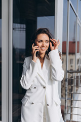 Pretty stylish business woman stands on the balcony near modern office and talking on the smartphone.