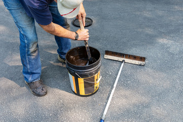 Stirring  bucket of asphalt sealer before using on driveway