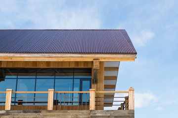 Detailed view of wooden house with large window under the blue sky. The house is made of wood and glass in the modern style.