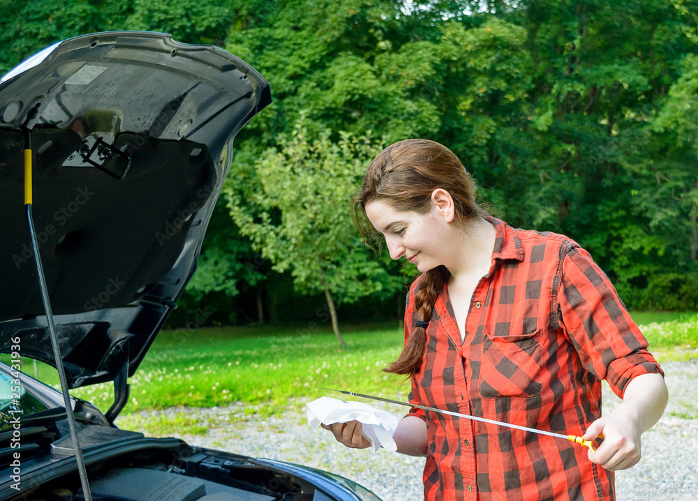 Wall mural Young woman checking motor  oil dipstick