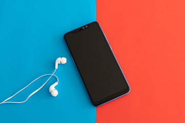 Black Smartphone with White Handsfree Isolated on a Red and Blue Background