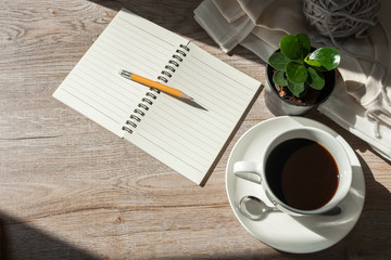coffee cup, pencil and notebook on wooden in the morning light.