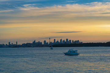 Fototapeta premium Colourful sunset over harbour with yachts and Sydey cityscape in the distance