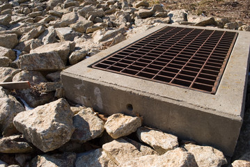 Metal storm grate in concrete and stones