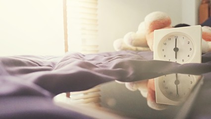 Alarm clock (6 o' clock in the morning) on the bed at home. Morning time background concept, soft focusing and vintage color style.