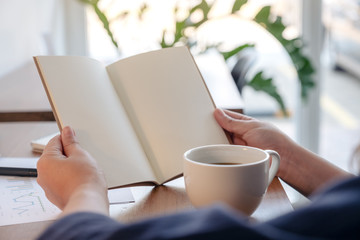 Closeup image of a woman holding and opening a blank notebook with coffee cup and papers on the table