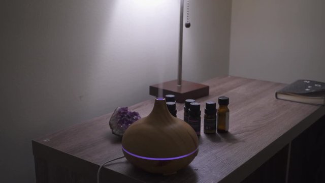 Essential Oil Diffuser misting with changing colors. On desk next to amethyst crystal. New Age Bedside Altar