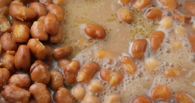 Close video of fava beans and broth in a pan boiling while heating illuminated with natural lighting.