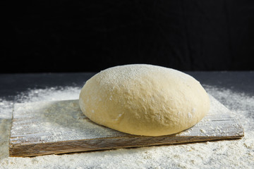 Fototapeta na wymiar Pizza dough or baking on a dark black background of wood. Baking bread, pizza, pasta. Top view, horizontal photo