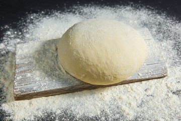 Pizza dough or baking on a dark black background of wood. Baking bread, pizza, pasta. Top view, horizontal photo