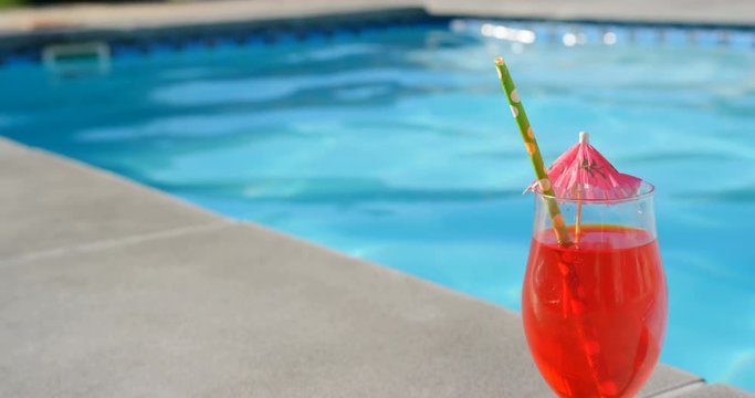 Close-up of cocktail glass with umbrella and straw near swimming pool 4k