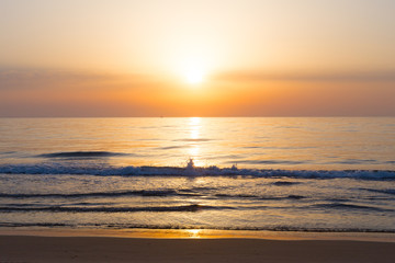 Fototapeta premium Sunrise at sandy Mediterranean Sea beach with splashing wave. Sunrise over the sea with reflections and sailboat on the horizon.