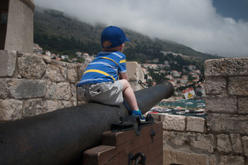 Boy sitting on historic cannon in old European fortress