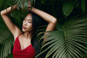 Fototapeta na wymiar Fashion. Asian woman model in red dress with green palm leaves