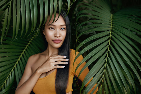 Hair beauty. Woman model with long straight hair in palm leaves