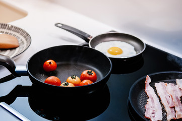 Cooking breakfast pan grilled tomatoes, bacon and fried  egg