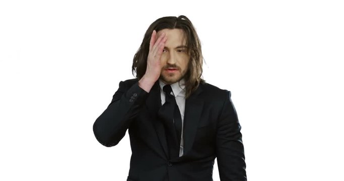 Portrait shot of the handsome young Caucasian man with long hair in the suit and tie looking very tired while standing on the white background.