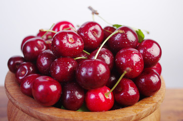 Sweet cherry fruits with leaves in a wooden bowl on a white background