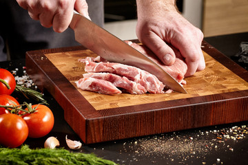 Closeup of male hands with a knife cut a piece of raw meat