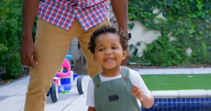 Front view of young black father and little son playing in back yard of their home 4k
